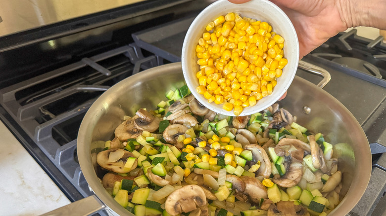 hand adding corn to pan with veggie medley