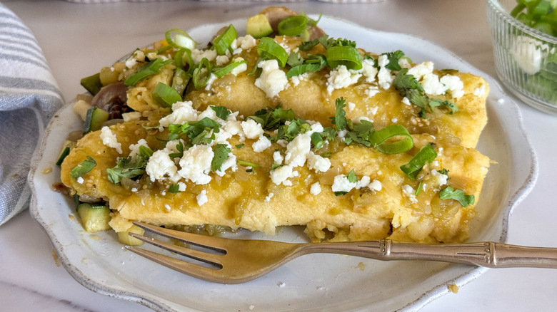 enchiladas verdes on plate with green onions and queso fresco