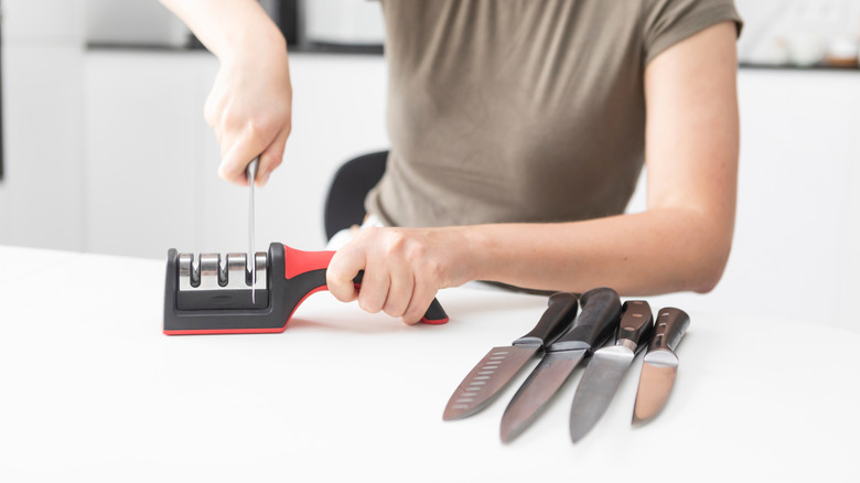 A woman sharpening a set of knives on a knife sharpener