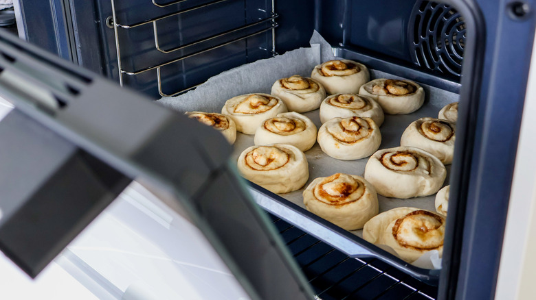Placing a tray of cinnamon rolls lined with paper into an oven