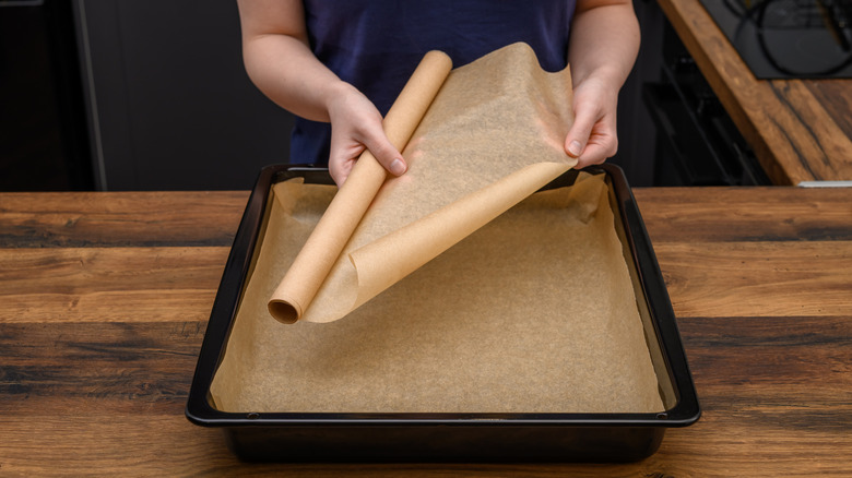 Someone unrolling a sheet of wax paper and lining a baking pan with it.