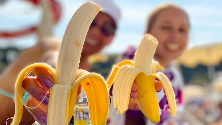Two women holding peeled bananas