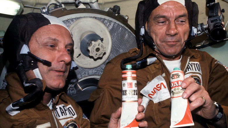 Astronauts Thomas P. Stafford (left) and Donald K. "Deke" Slayton hold containers of Soviet space food in the Soyuz Orbital Module, 1975