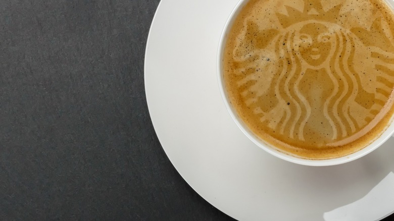 Cup of coffee with Starbucks Mermaid logo stenciled into the top