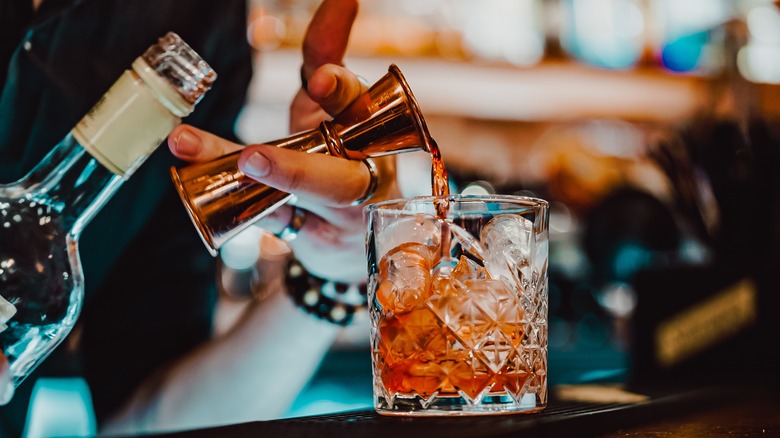 Pouring red liquor from a cocktail jigger into rocks glass.