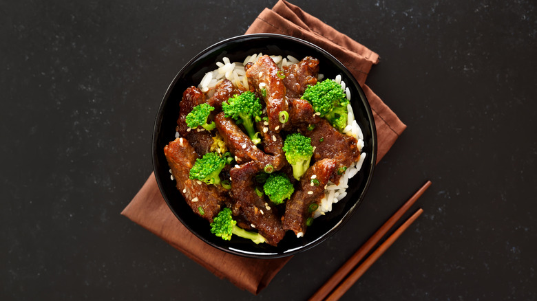 Beef and broccoli stir fry in black bowl with chopsticks, overhead view