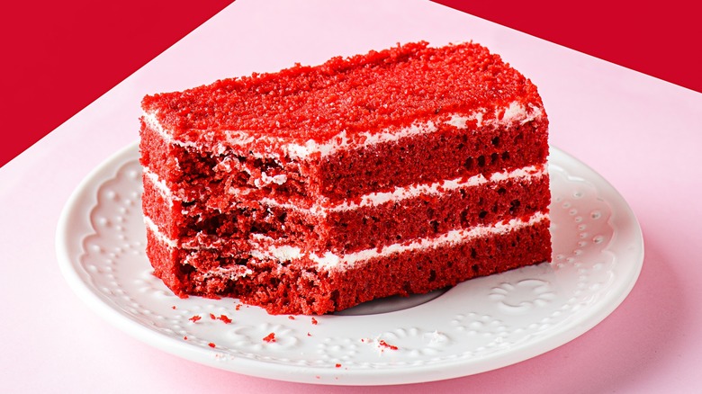 rectangular slice of red velvet cake on a white plate against a pink and red background