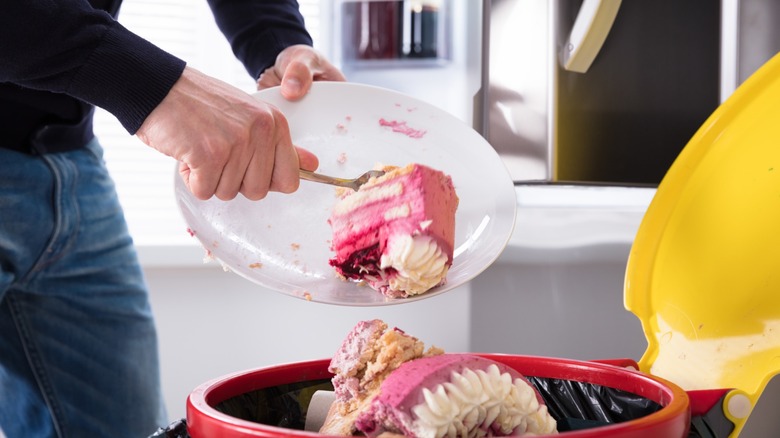 a hand scoops decorated cake into the trash