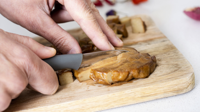 Hands cutting seitan on a wooden cutting board