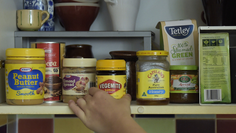 Hand reaching for jar of Vegemite inside a cupboard.