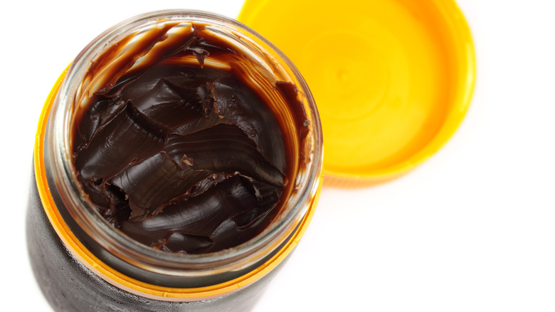 Thick, brown Vegemite spread inside a clear jar. 