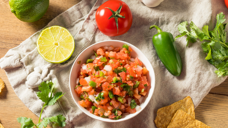 Pico de gallo in a bowl next to cilantro and lime