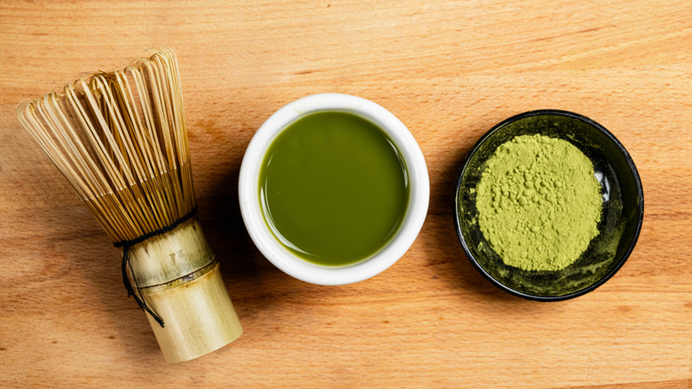 A bowl of green matcha tea with matcha powder and a traditional matcha whisking tool