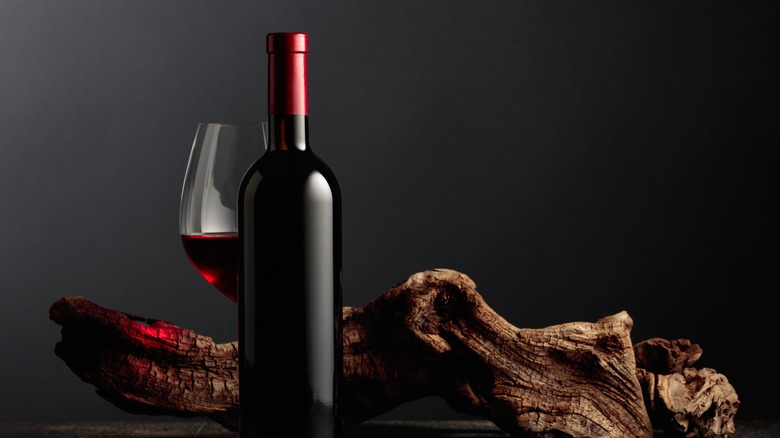 bottle and glass of red wine in front of a piece of driftwood and a black background