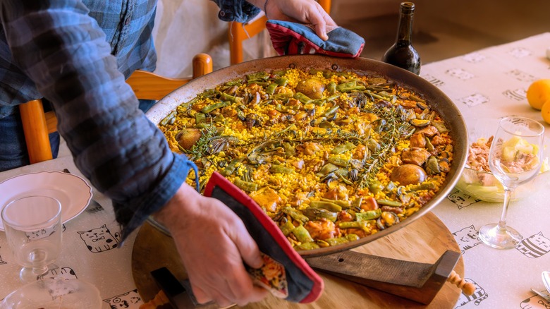 Hands place a pan of paella on a table