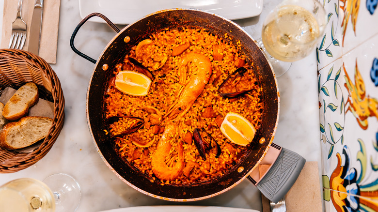 A pan of paella is studded with citrus, prawns, and mussels