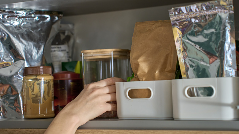 Person takes jar from kitchen shelf filled with food containers