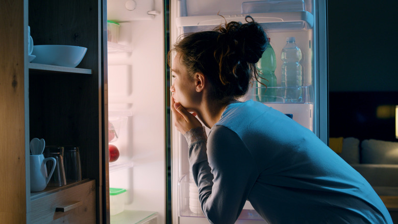 Woman looking into fridge, dark background, side view