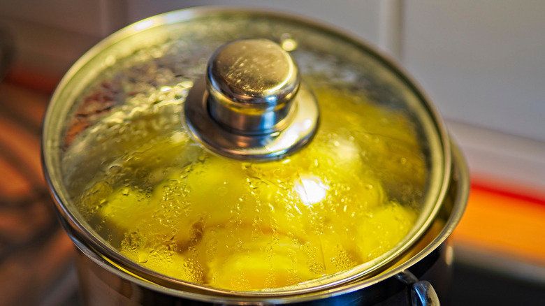 A pot of boiling potatoes on the stove with the lid slightly askew