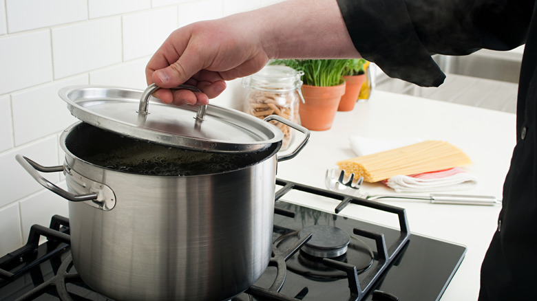 Someone lifting the metal lid off a pot of boiling water
