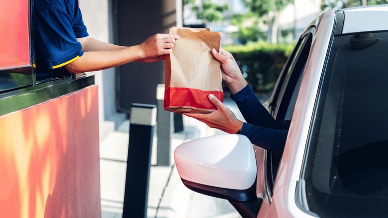 worker hands mcdonald's bag out drive-thru window