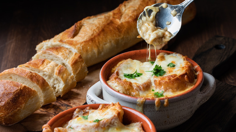 Two bowls of French onion soup with melted Gruyere, a spoon, and a baguette