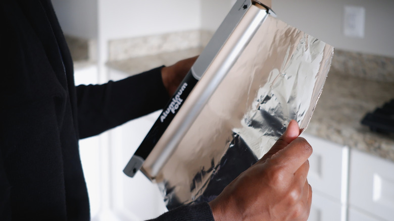 A close-up of someone unrolling aluminum foil from a roll