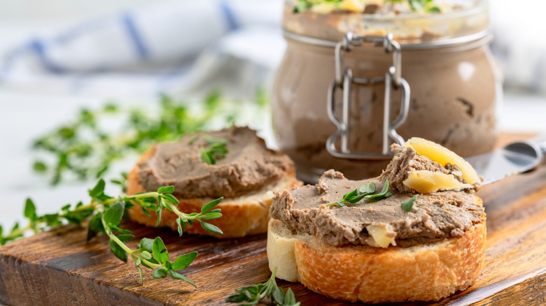 Slices of bread topped with pate on a wood cutting board, with a jar of pate in the background