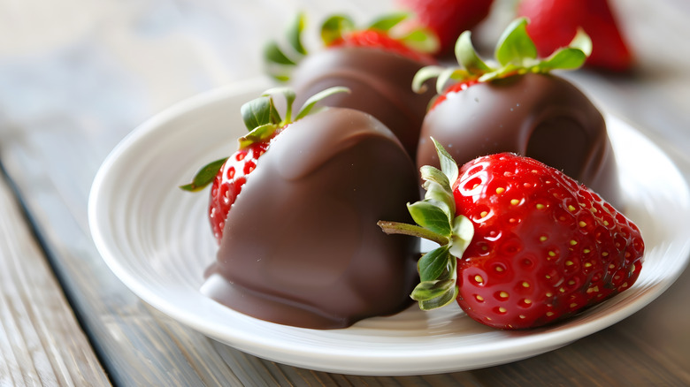 One plain strawberry and three dipped in chocolate on white plate