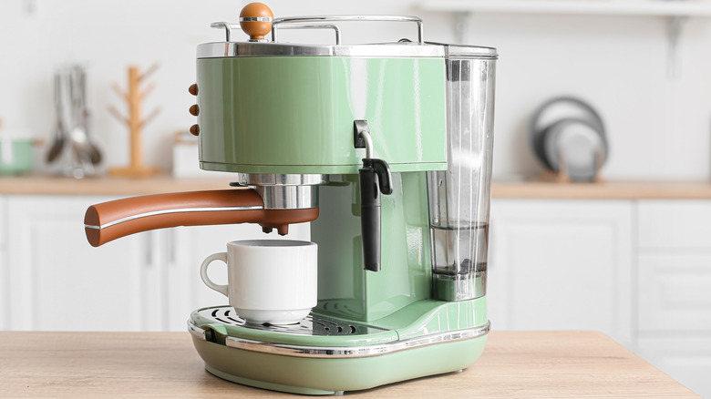Modern coffee machine with cup on table in kitchen