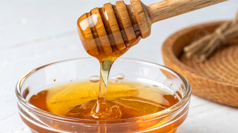 Honey being drizzled from a honey wand into a small glass bowl