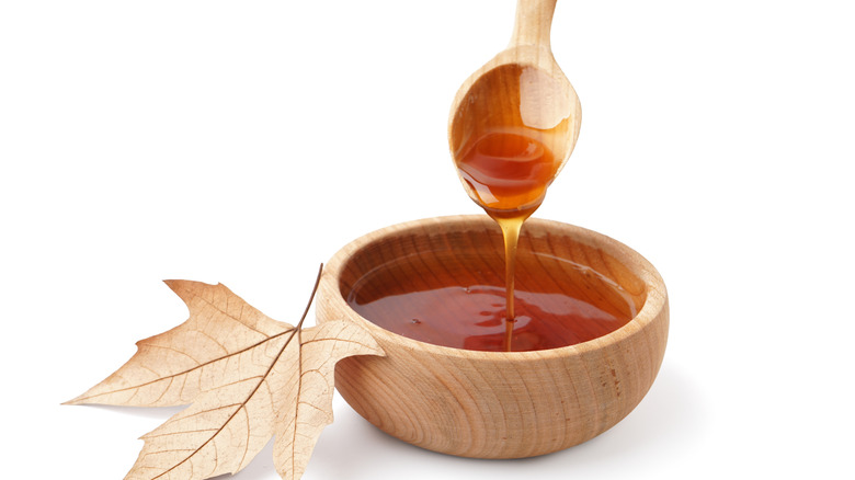 Maple syrup being poured from a spoon into a small wooden bowl