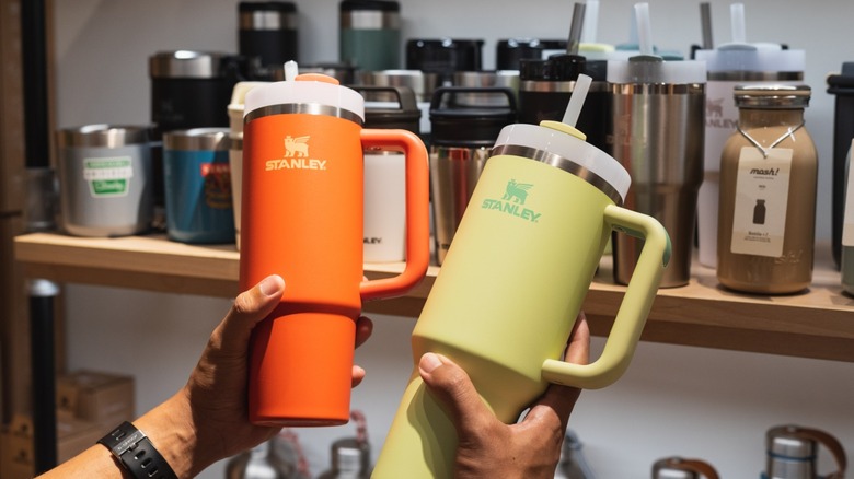 hands hold a pair of colorful stanley mugs