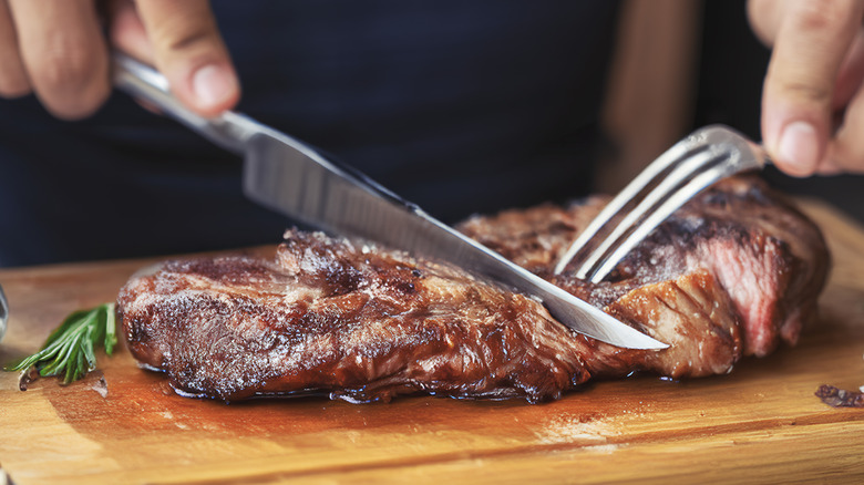 Someone cutting meat with a steak knife