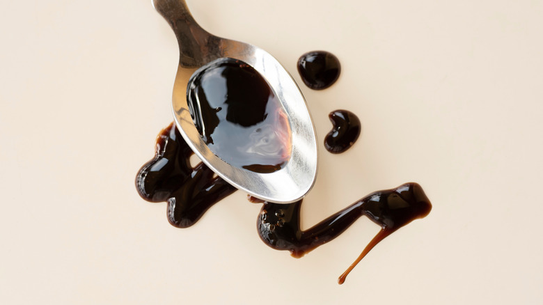 A spoon drizzles balsamic vinegar on white surface