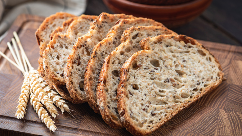 Whole wheat sourdough bread sliced on a wooden cutting board, with a few wheat stalks to the side
