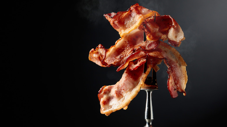 Cooked bacon held up on a two-pronged fork