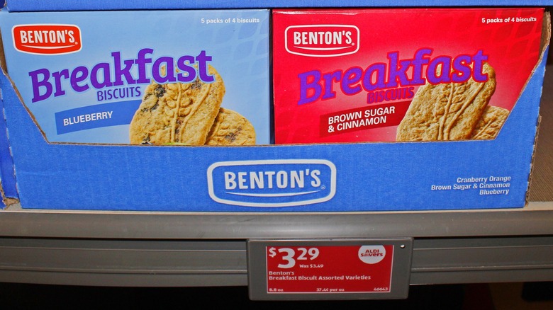An image of an old, red Aldi price tag, which reads $3.29 for Benton's breakfast biscuits, posted on a metal shelf under blue and red packages of the biscuits themselves.
