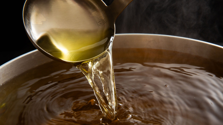A metal ladle pouring broth into a giant metal pot