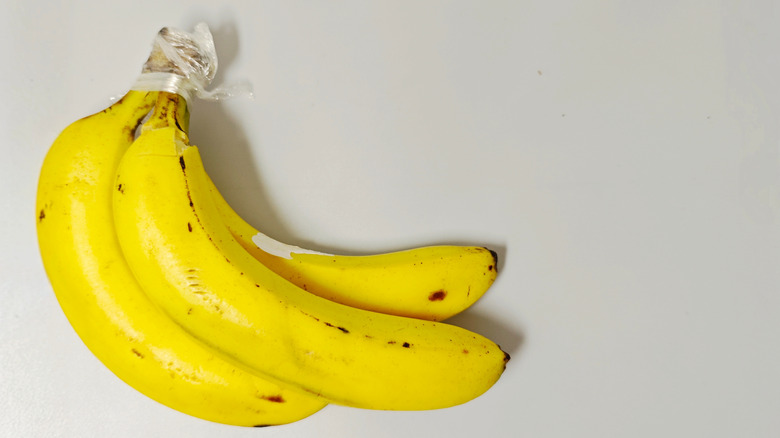 A close-up of three ripe bananas with plastic wrapped around the stems