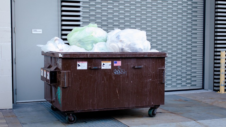 brown dumpster wth plastic bags up top