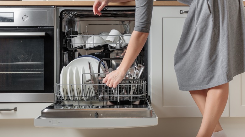 A shot of a woman opening a full dishwasher