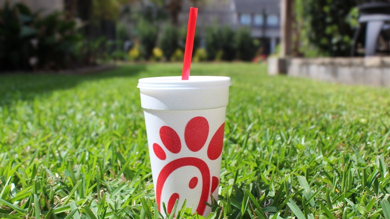A white Chick-fil-A drink cup with a red straw sitting in green grass