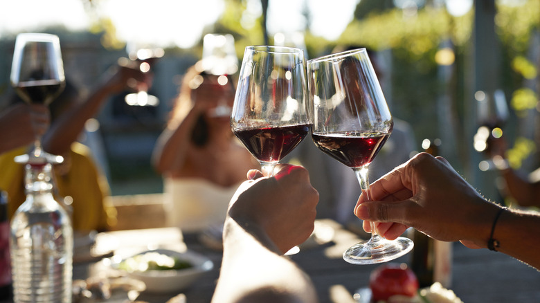 A close-up of two wine glasses among a group of people drinking red wine together