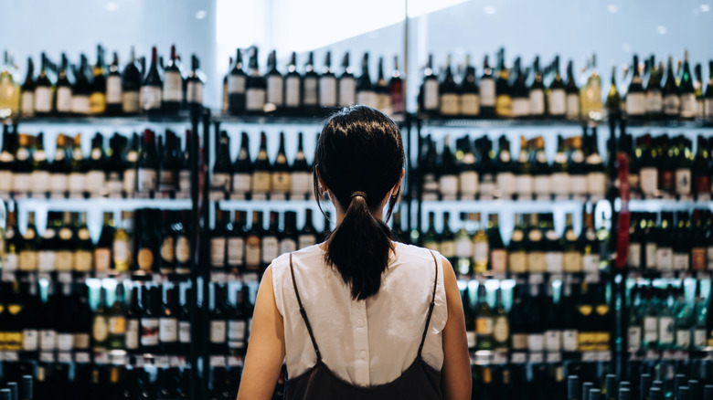 A woman standing in the liquor aisle of a store, staring at the wide selection of wine available