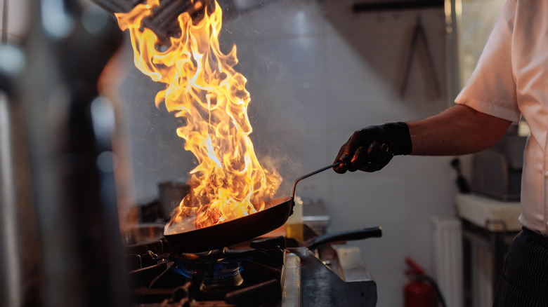 Chef flambeing food in a pan over high heat