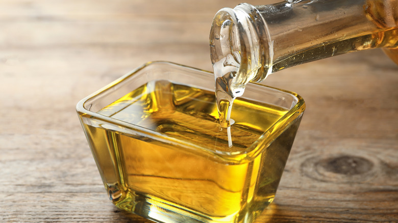 Pouring cooking oil from jug into bowl on wooden table