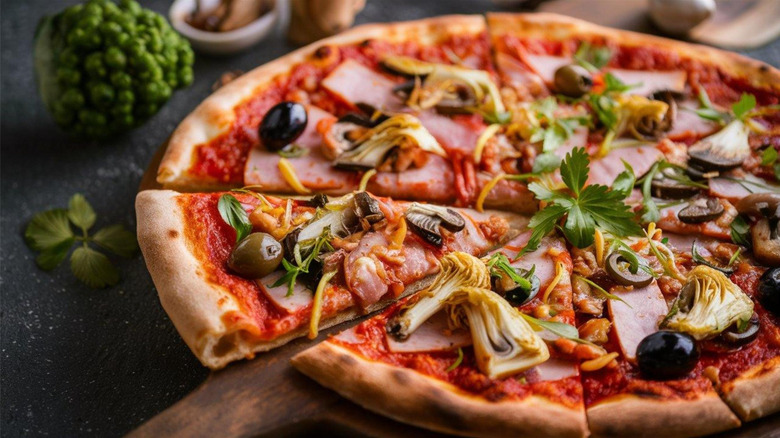 Cheeseless pizza with ham, olives, herbs, and other ingredients on a wooden pizza peel