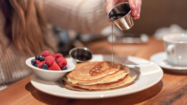 Woman in diner pouring syrup on plate of pancakes