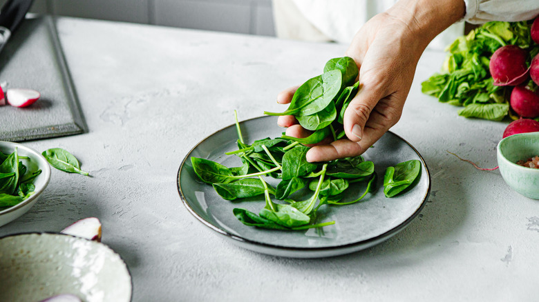 Someone scooping spinach leaves out of a plate with their hand